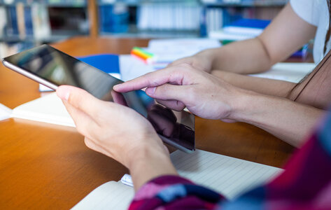 Bildausschnitt: Zwei Personen arbeiten mit einem Tablet im Klassenzimmer. Es sind nur die Hände erkennbar.