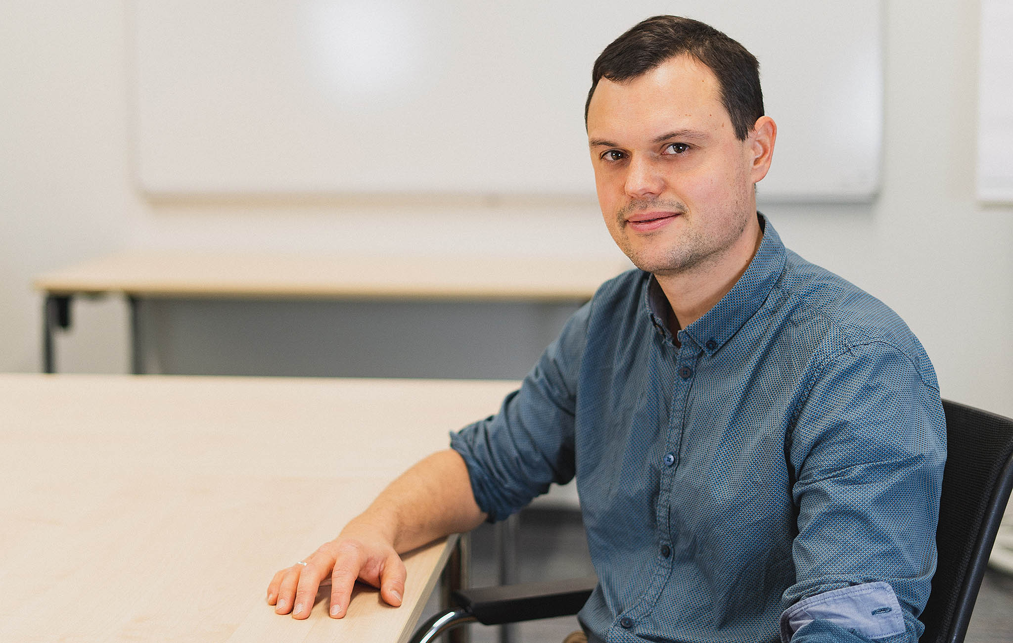 Der Lehrer Alexander Vötterle sitzt am Schreibtisch und lächelt beim Interview in die Kamera. 