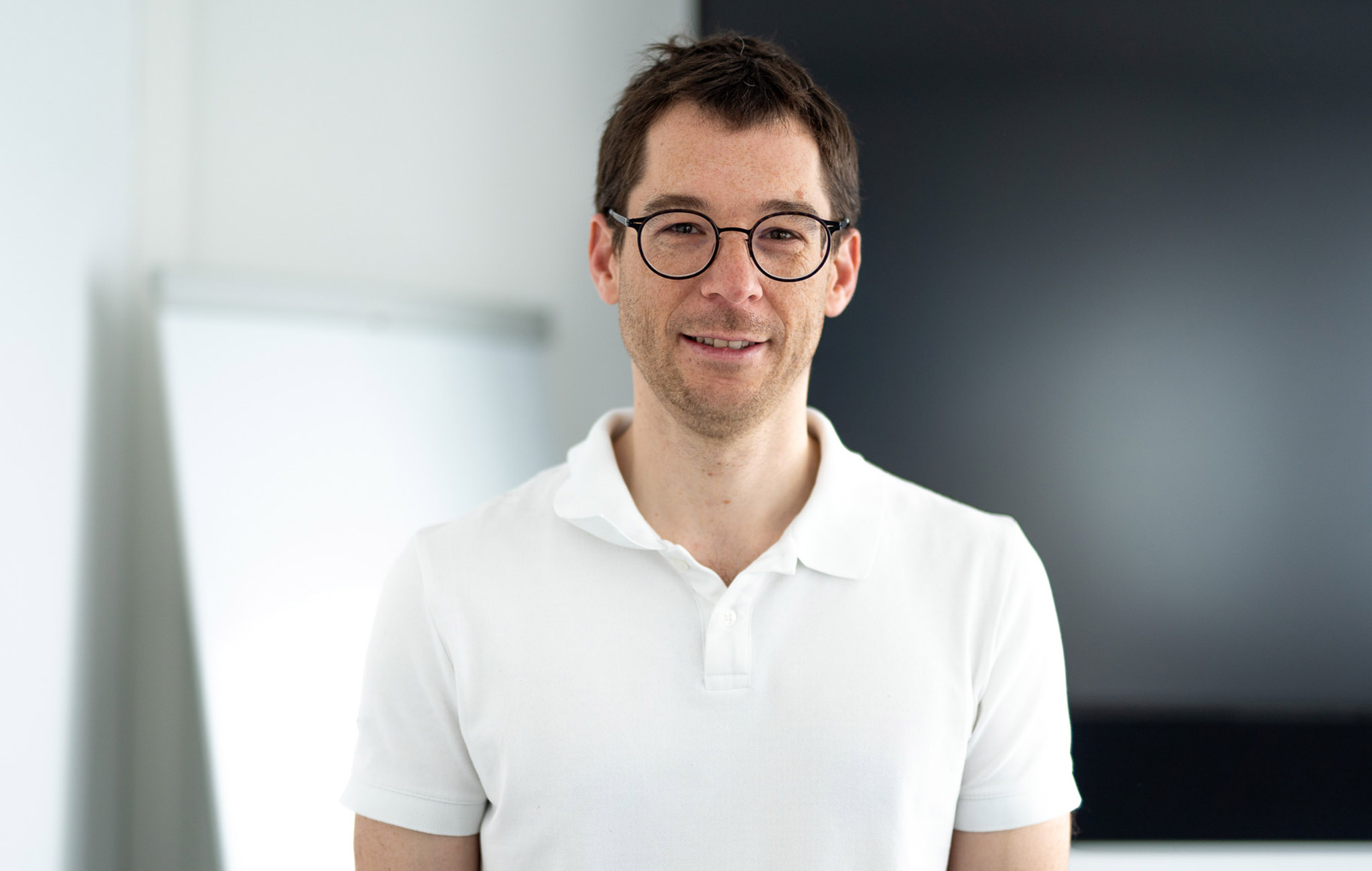 Lehrer mit weißem Poloshirt steht vor Flipchart.