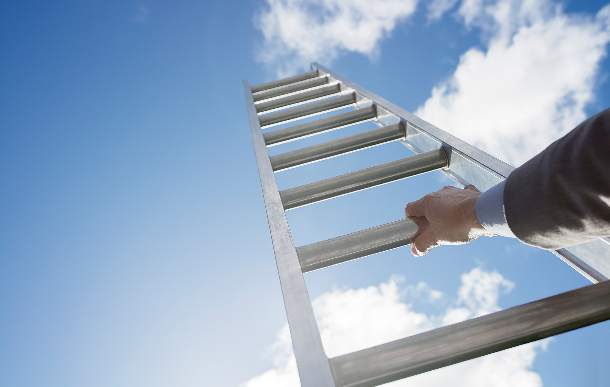 Symbolbild zur Weiterentwicklung der paedML: Eine Hand greift nach einer Metallleiter in den Himmel, vor blauem Himmel mit Wolken im Hintergrund.