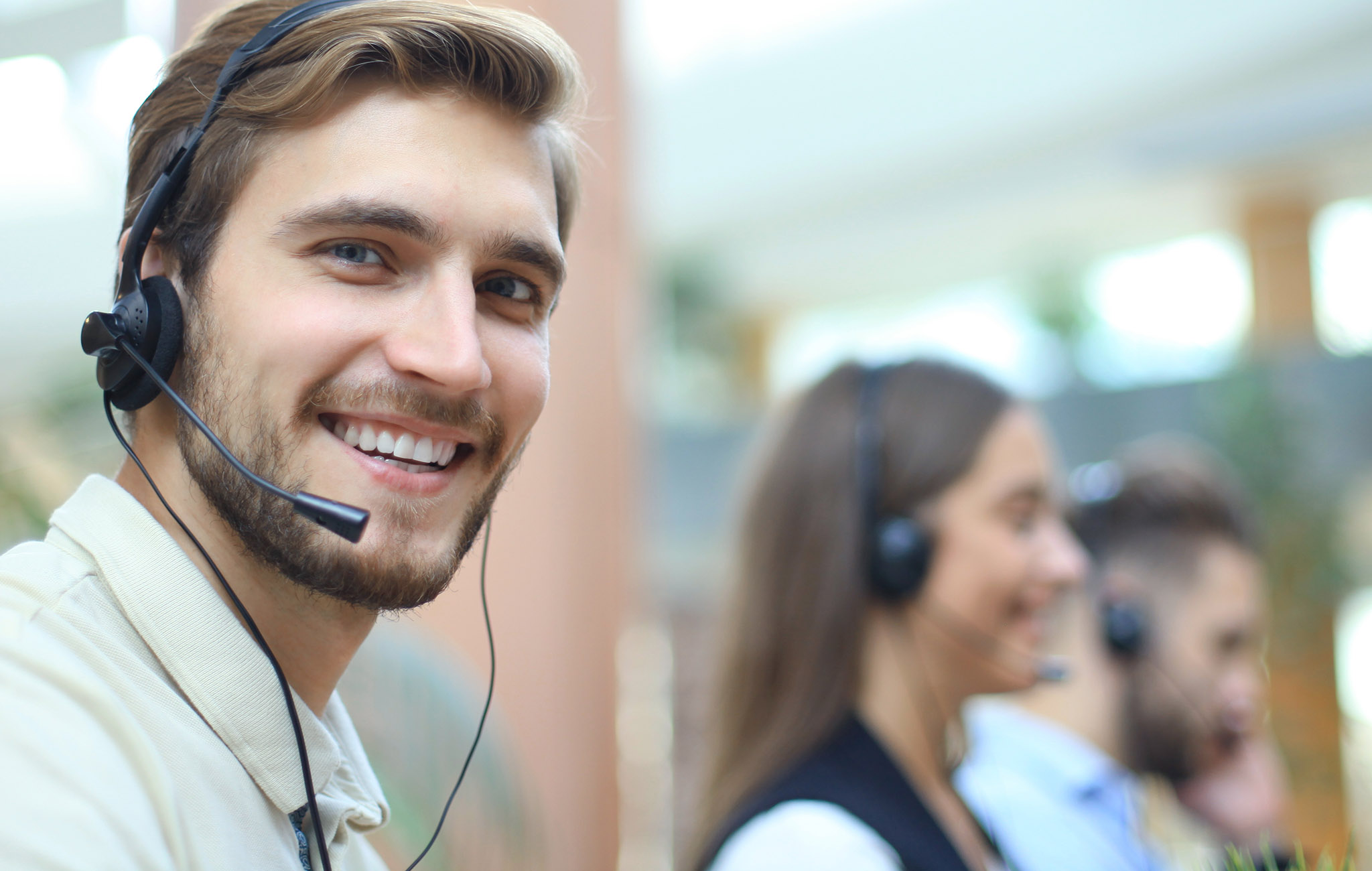 Freundlicher, junger Mann mit Headset beim Telefon-Support.