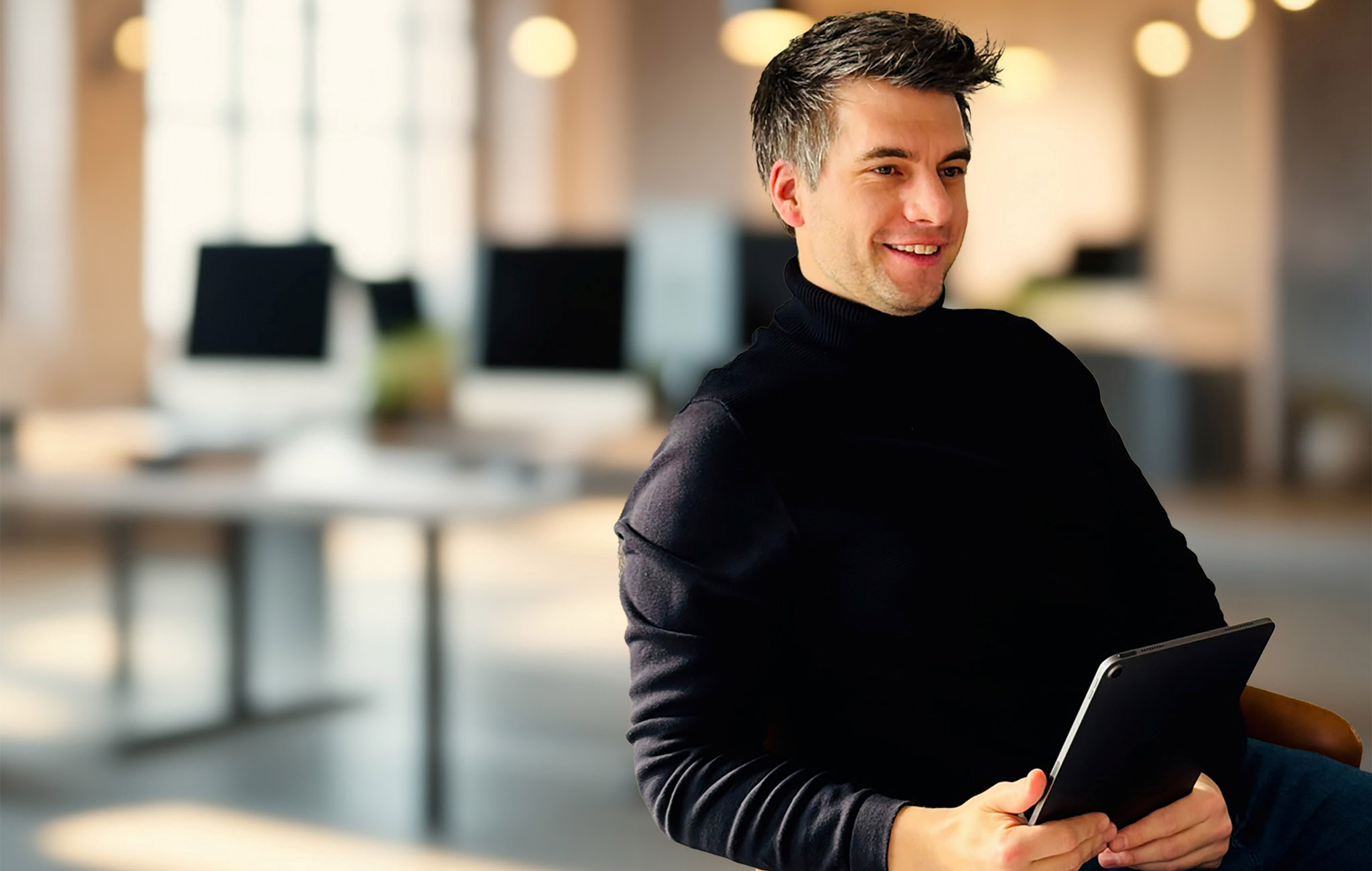Porträtaufnahme eines lächelnden Mannes mit Tablet in der Hand, aufgenommen in einem modernen Büro – Symbolbild für digitale Schulverwaltung mit paedML.