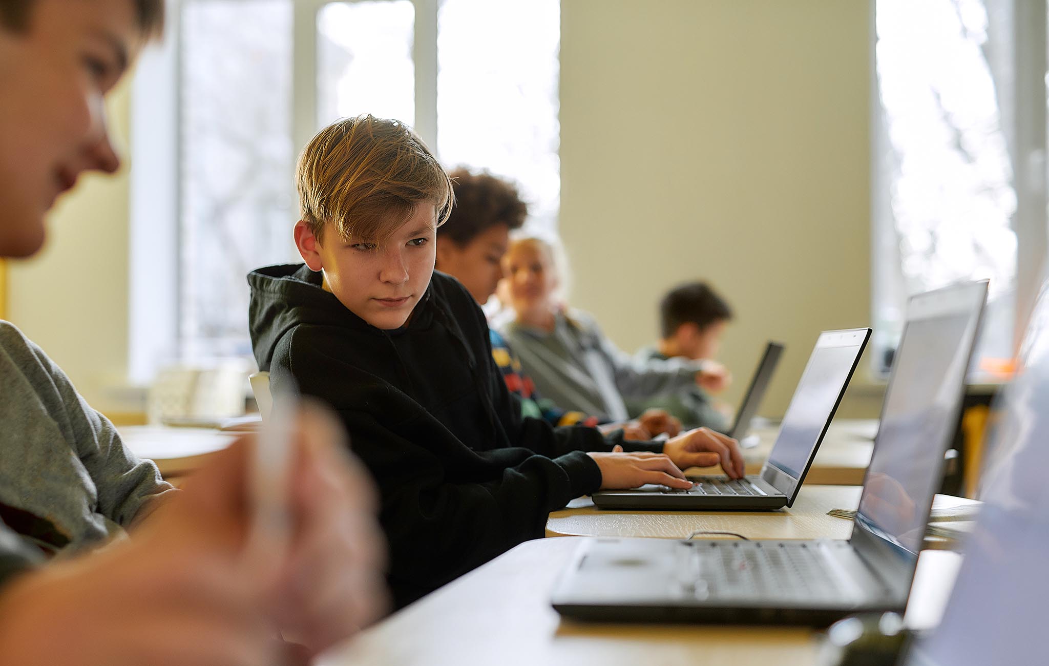 Schüler sitzt mit Laptop im Klassenzimmer, konzentrierter Blick auf den Bildschirm – Symbolbild für Einsatz moderner Schul-IT mit paedML Linux und OPSI.