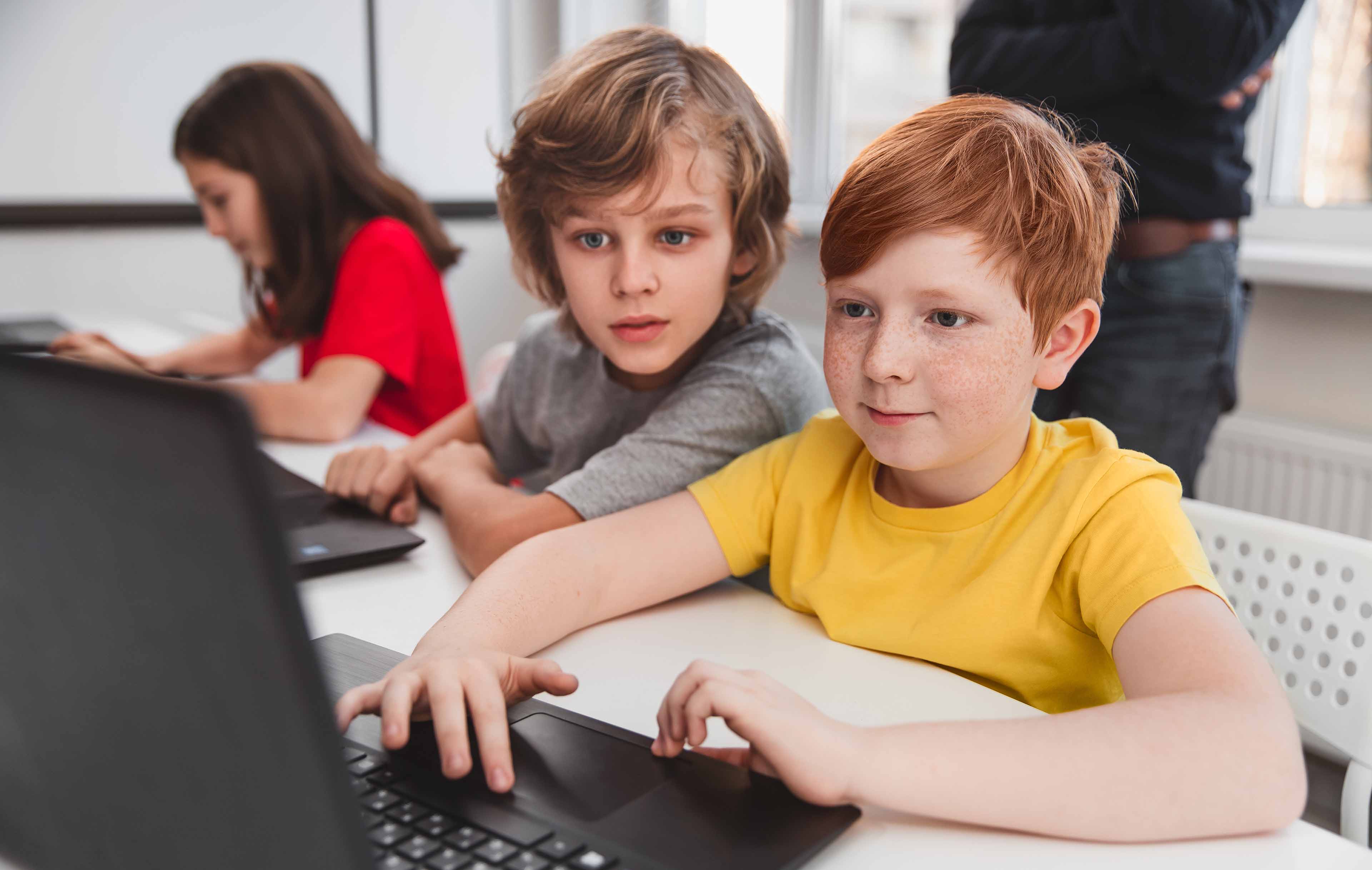 Foto von Grundschulkindern im Klassenraum, die gemeinsam an einem Laptop arbeiten – Symbol für digitale Medienbildung mit paedML im Schulalltag.