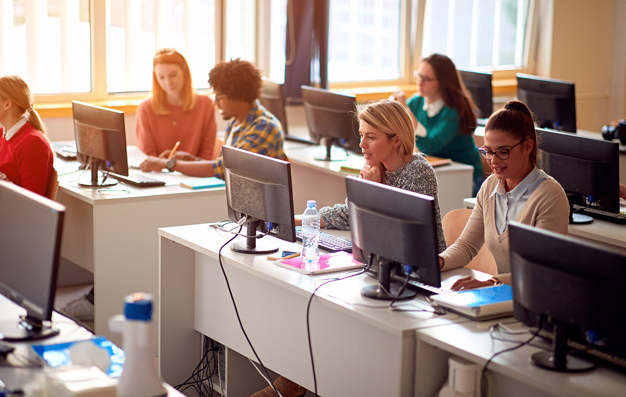 Klassenraum mit vernetzten Computern mehreren Studentinnen und Studenten am Arbeiten.