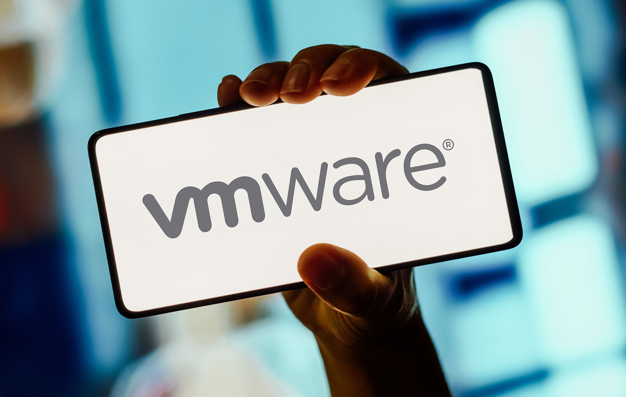 Hand hält Smartphone mit dem Logo von VMware vor unscharfem Hintergrund – Symbolbild für Virtualisierungslösungen in der Schul-IT mit paedML