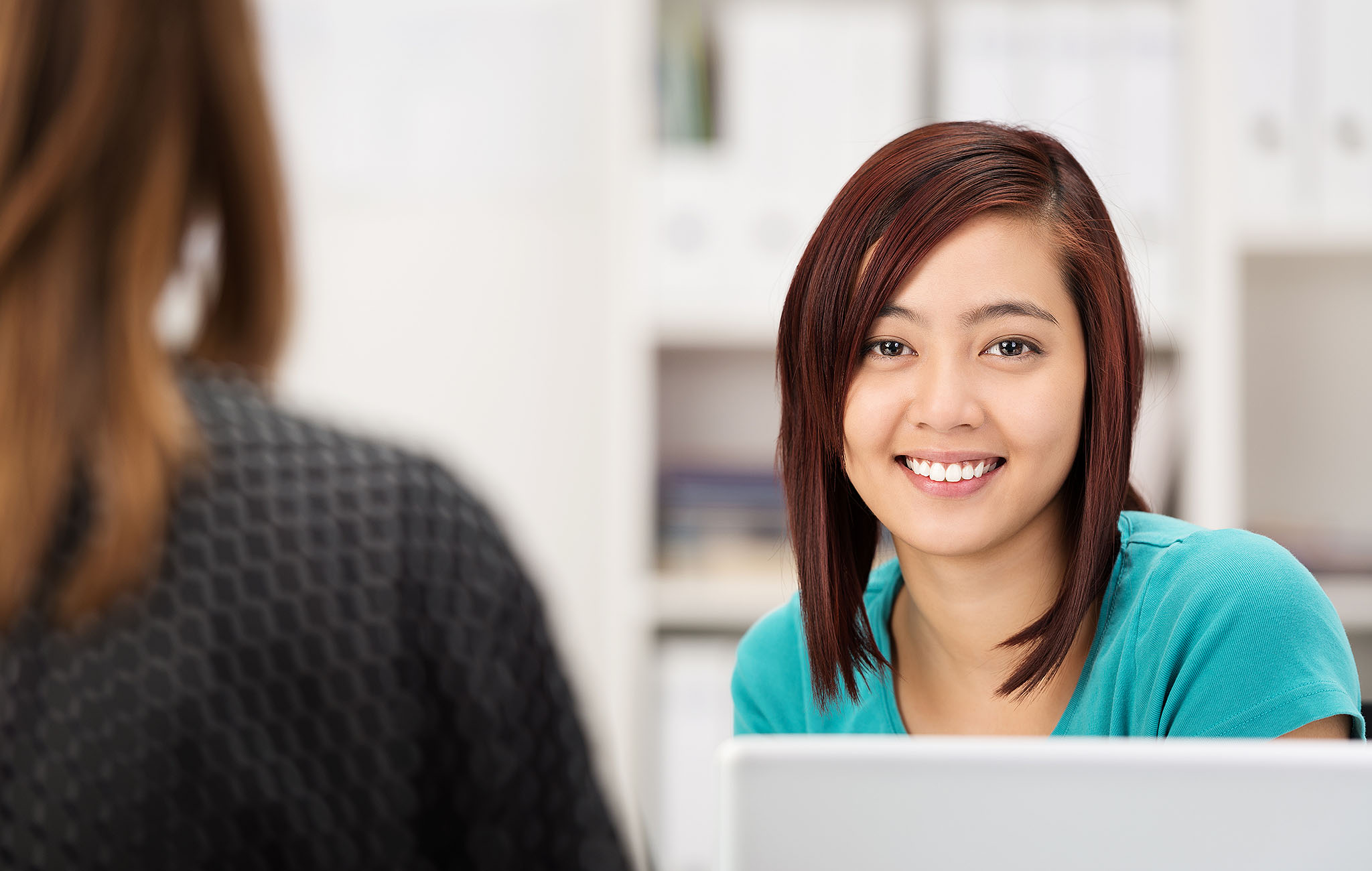 Junge Frau sitzt mit Laptop in einem modernen Büro und lächelt – Symbolbild für nutzerfreundliche IT-Verwaltung mit dem neuen HUB in paedML Windows.