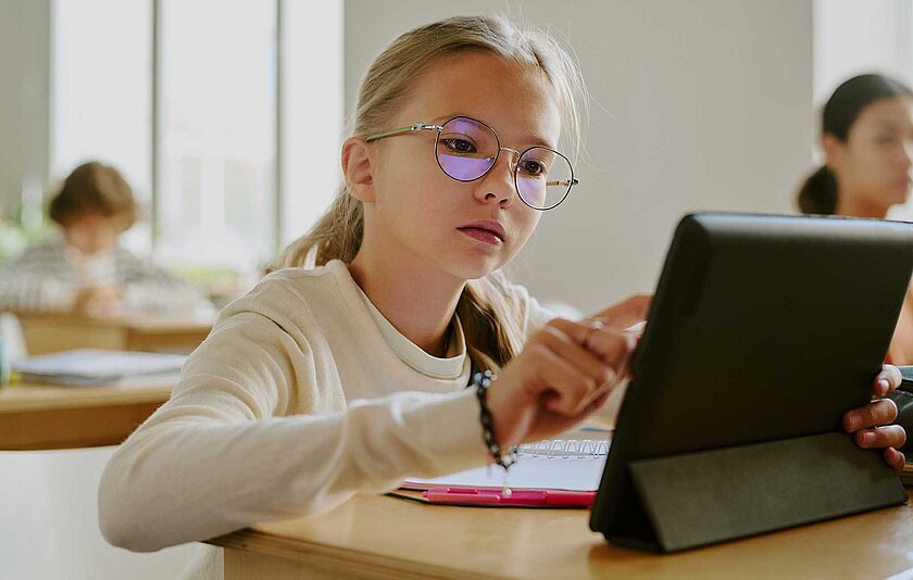 Schülerin mit Brille arbeitet konzentriert mit einem Tablet im Unterricht.