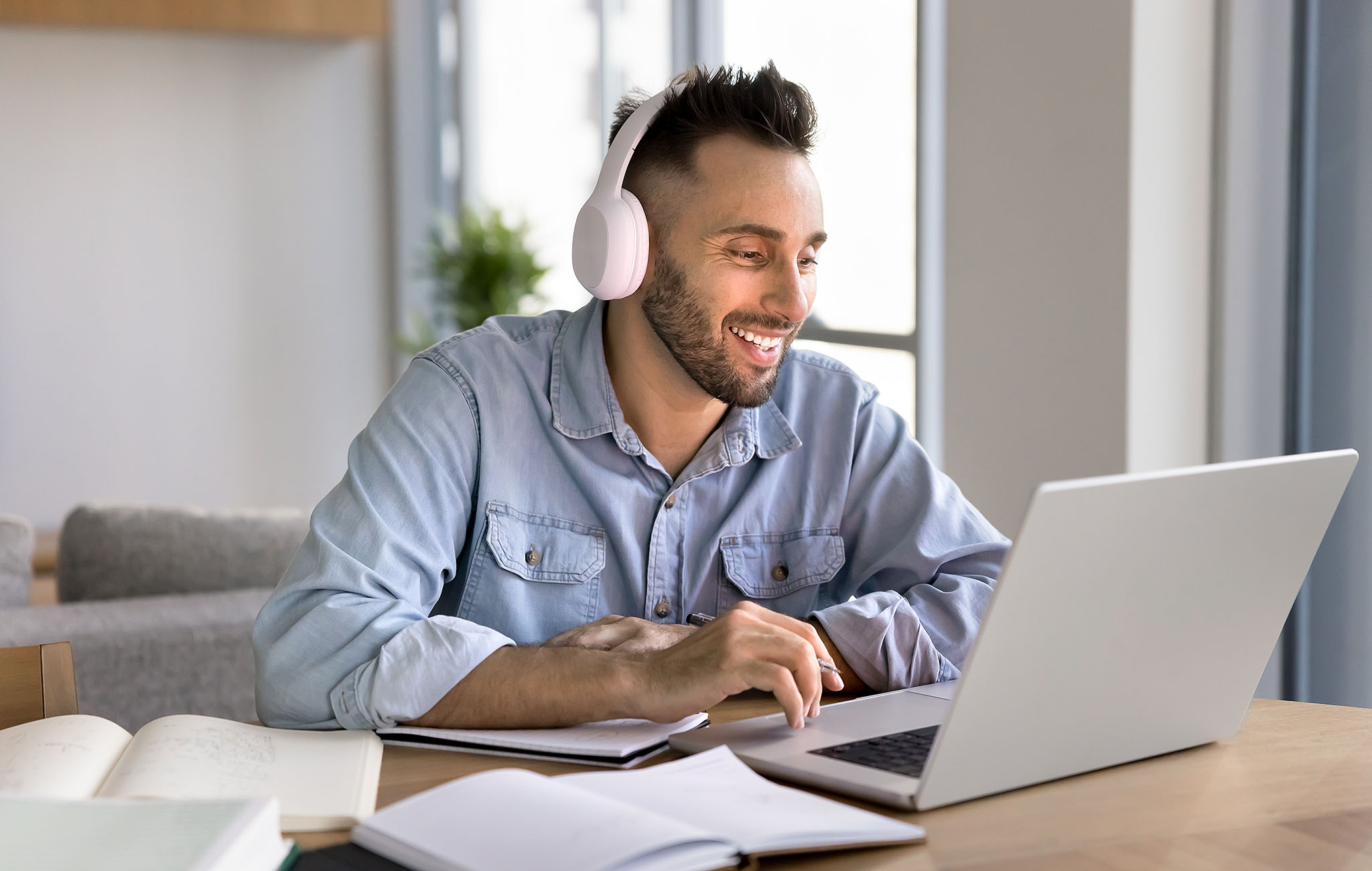 Junger Mann arbeitet am Laptop mit Headset und lächelt. Vermutlich ist er mit einem Tutorial beschäftigt.