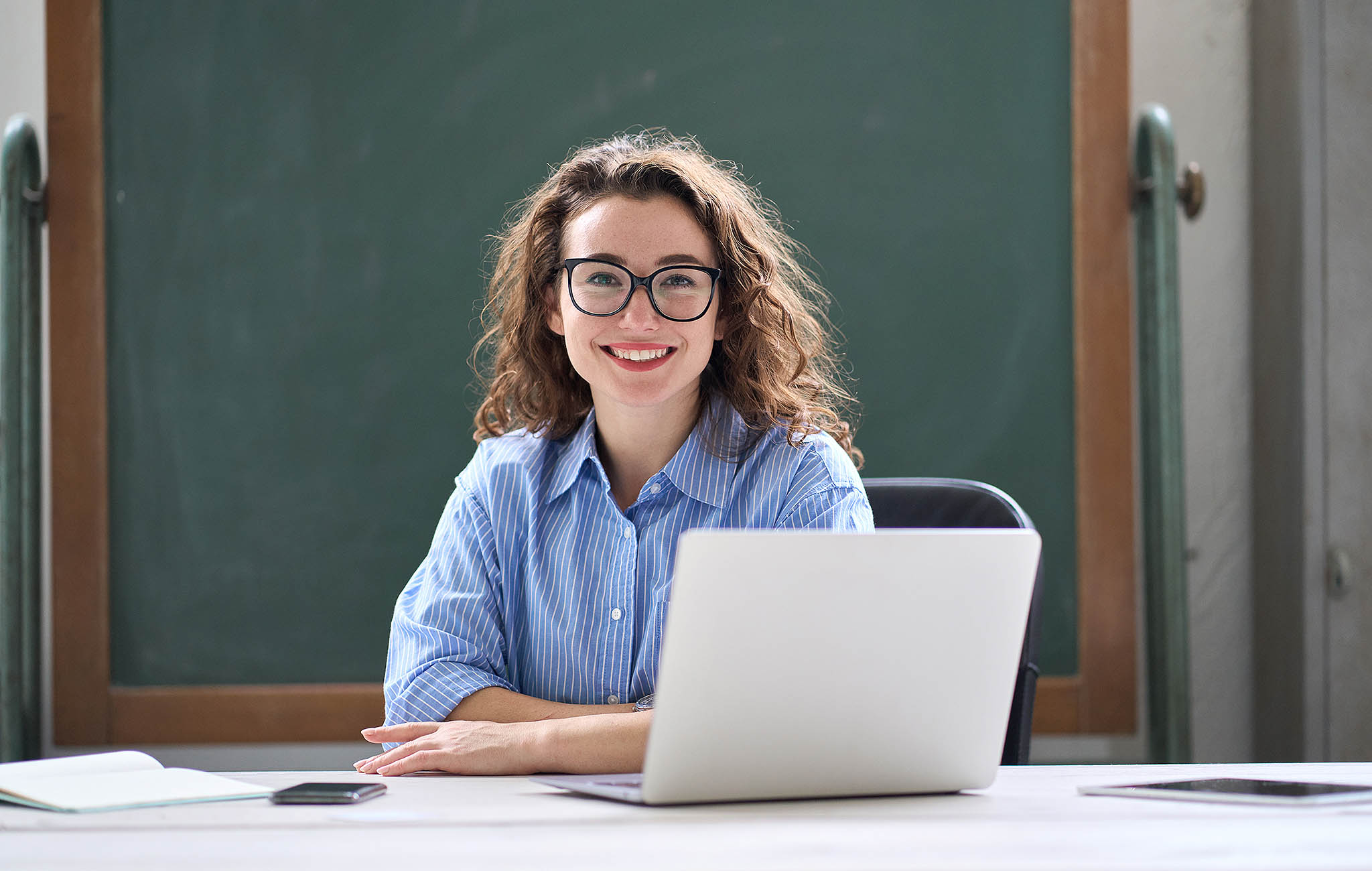 Lehrerin mit Laptop vor grüner Tafel – steht symbolisch für praxisnahe IT-Administrationswerkzeuge in der paedML Novell-Schulkonsole